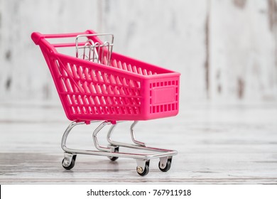 Miniature Pink Toy Shopping Cart On White Wooden Background