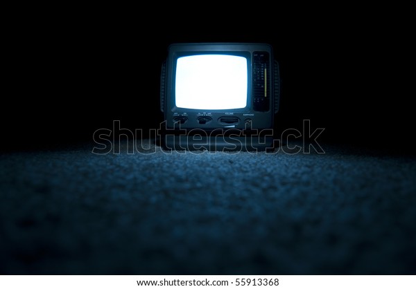 A miniature portable TV screen on at night\
on the floor with a white screen\
glowing