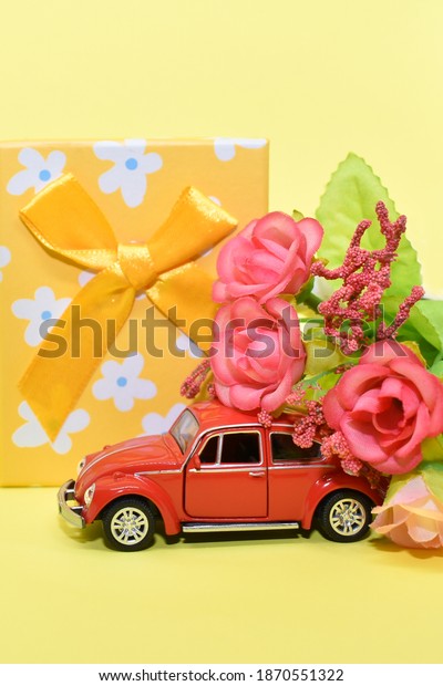 Miniature red car, flowers and gift box. Red retro\
car delivers bouquet and gift box on yellow background. Valentine,\
postcard for March 8, Mother\'s Day, birthday. Novosibirsk,\
Russia-November 8,\
2020