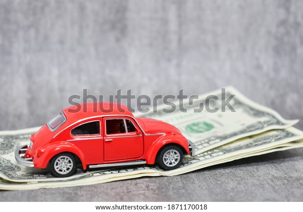 miniature red car on the background of us dollars\
banknotes. Red toy car and money on gray background. Savings\
concept, car loan, gasoline prices and car insurance.\
Novosibirsk,Russia-December 8,\
2020