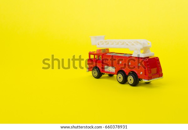 miniature red color fire truck on\
yellow background, toy car, selective focus, copy\
space