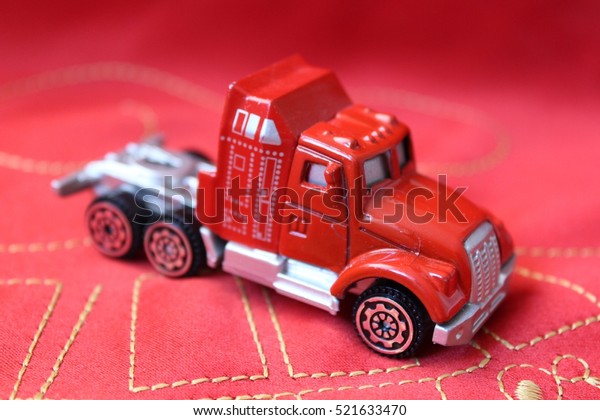 Miniature red toy truck sitting on red
textile material stitched with golden string macro shot
