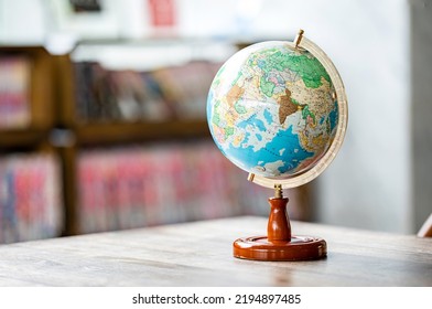 A miniature replica of the globe is placed on wooden table beside bookshelf in the library. - Powered by Shutterstock