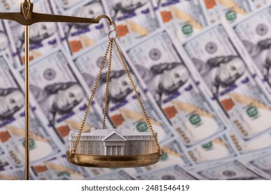 A miniature residence of the President of the United States, the White House, on the scales against the background of 100 US dollar bills - Powered by Shutterstock