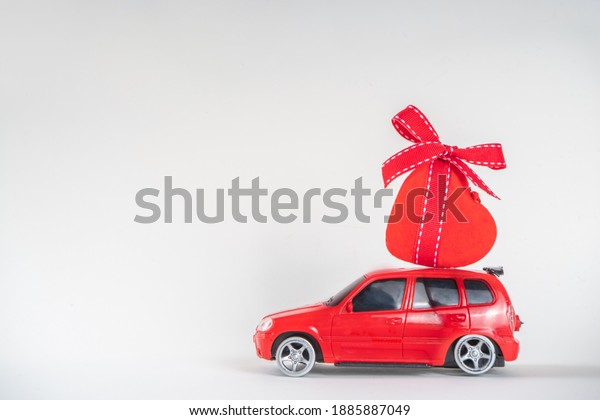 Miniature retro toy red car carrying red heart\
decor, on white background copy space. Valentine day concept,\
greeting card\
background