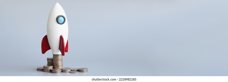 Miniature rocket stand on stack of coins, rocketship as symbol to open business project