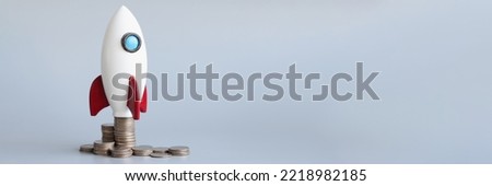 Miniature rocket stand on stack of coins, rocketship as symbol to open business project