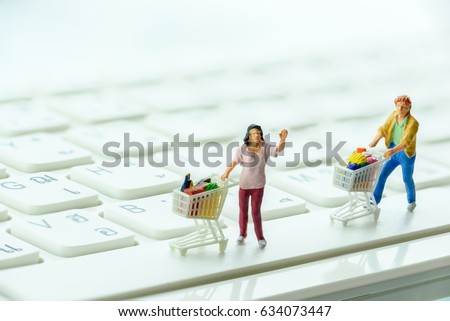 Miniature shoppers push a shopping cart on a keyboard. Concept of decreasing in foot traffic after the coming of online internet ecommerce. E-commerce gives many choices to customers at lower price.