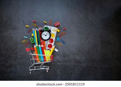 miniature shopping cart with accessories, stationery set and alarm clock on abstract dark background. Back to school, education concept. symbol of creativity, artistic art. top view. copy space - Powered by Shutterstock