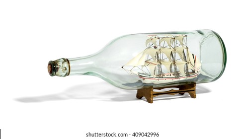 Miniature Tall Ship With Sails Rigged In A Clear Glass Bottle Displayed On A Small Wooden Stand Over A White Background In A Nautical Theme