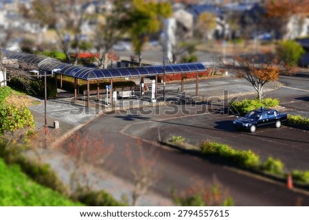 Miniature tilt-shift effect of a bus stop station and a black taxi car parked on the asphalt road