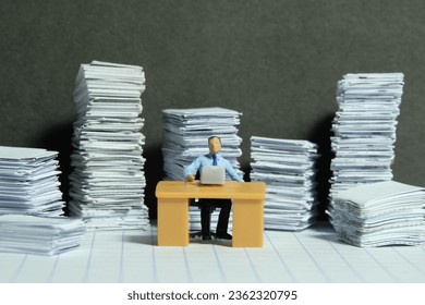 Miniature tiny people toy figure photography. Overload and work overtime concept. A businessman seat on a desk with pile of document. Image photo