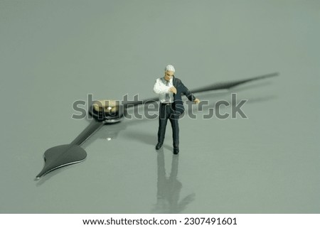 Miniature tiny people toy figure photography. Go to work concept. A businessman getting ready wearing suit in front of clockwise. Isolated on grey background. Image photo