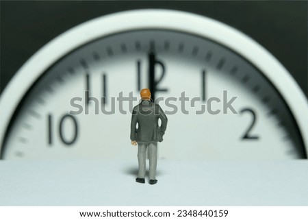 Miniature tiny people toy figure photography. A businessman standing in front of clockwise. Image photo