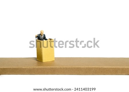 Miniature tiny people toy figure photography. A men with suit given speech standing at stage on tribune rostrum. Isolated on white background. Image photo