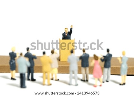 Miniature tiny people toy figure photography. A men with suit given speech standing at stage on tribune rostrum in front of audience crowd. Isolated on white background. Image photo