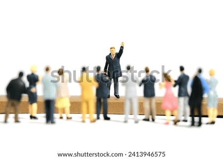 Miniature tiny people toy figure photography. A men with suit given speech standing at stage in front of crowd of audience. Isolated on white background. Image photo