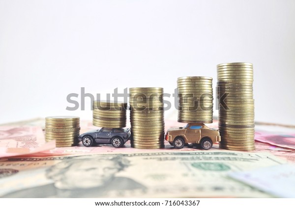 Miniature toy\
cars help carry coins between rolls ladder of gold coin money on\
various banknote in white\
background