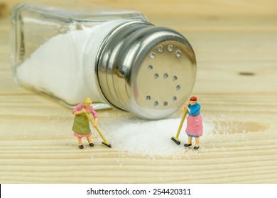 Miniature Toy Housewives Figures Cleaning Up Spilled Salt On Wooden Table