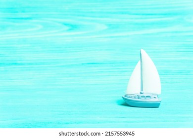 Miniature Toy Yacht On A Turquoise Wooden Table Background Imitating Water.