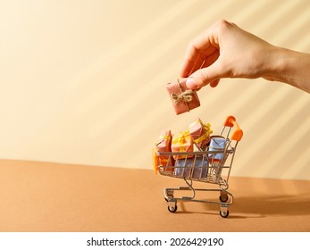 Miniature trolley with purchases, gifts. Beautiful packaging. A woman's hand holds one gift. Beige background. Discounts, sales, trade, Black Friday. - Powered by Shutterstock