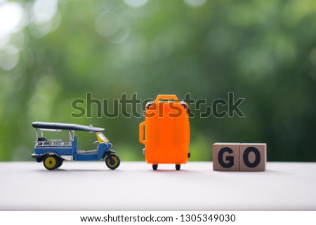 Miniature tuk-tuk and miniature orange suitcase with wood word GO, Travel in Thailand image concept