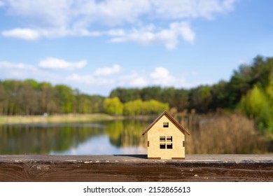 Miniature wooden cabin by against a beautiful lake landscape background. Lake cottage holidays concept.