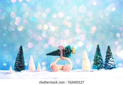 Miniature Wooden Car Carrying A Christmas Tree On A Shiny Blue Background