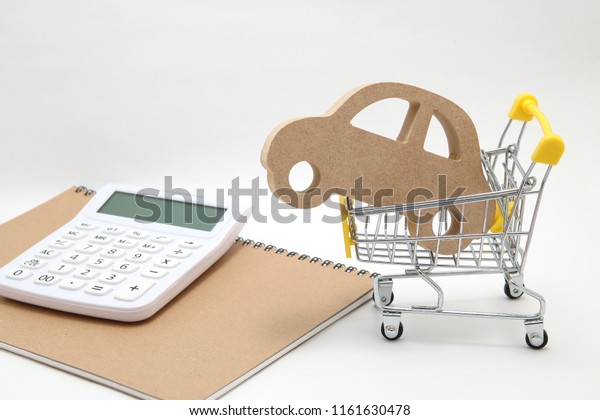 Miniature wooden\
car, shopping cart and  calculator on white background.\
Concept of\
buying new car.
