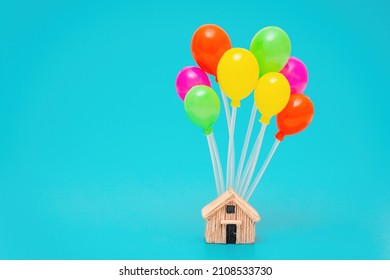 Miniature wooden house with a bunch of multicolored toy balloons isolated on a blue background. Home moving concept.