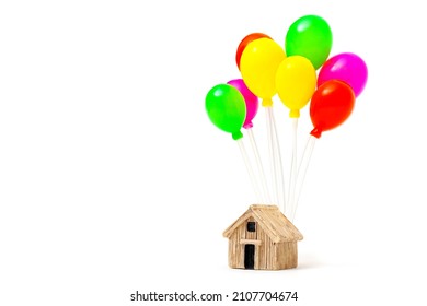 Miniature wooden house with a cluster of multicolored balloons isolated on a white background. Home relocation concept.
