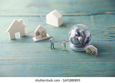 
Miniature Wooden House Model And Mannequins For Male And Female Business Model .Placed Near A Clear Round Piggy Bank.Concept Of Real Estate Investment And Saving Money For Home Purchase.