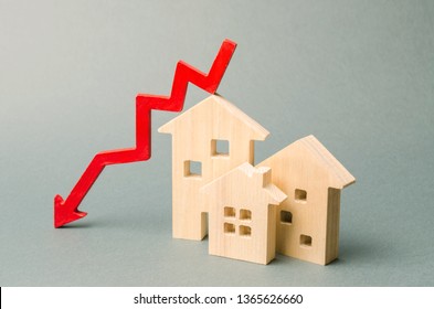 Miniature wooden houses and a red arrow down. The concept of low cost real estate. Lower mortgage interest rates. Falling prices for rental housing and apartments. Reducing demand for home buying