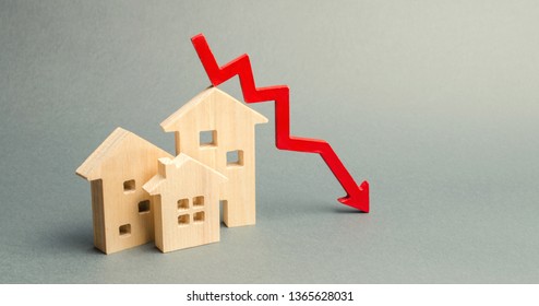 Miniature wooden houses and a red arrow down. The concept of low cost real estate. Lower mortgage interest rates. Falling prices for rental housing and apartments. Reducing demand for home buying