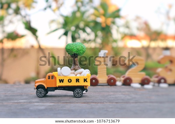 Miniature work truck carry white pills and tiny\
tree on wood table and blur wood craft number car in blurred\
natural tree bright\
light