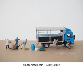 Miniature Worker Toys And Mini Diecast Truck On The Brown Table With White Background.