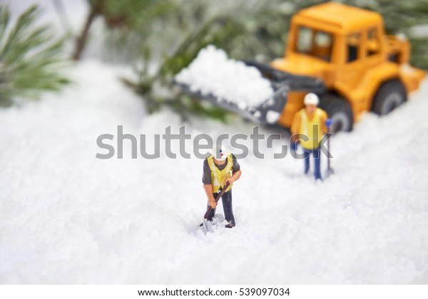 Miniature workers digging snow with yellow\
digger. Winter time. Holiday\
concept.