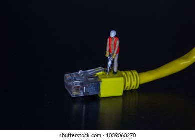 Miniature workman using a hammer drill on a yellow network cable and plug over a black background with copy space in a conceptual image