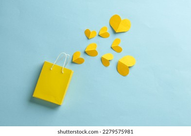Miniature yellow shopping bag with hearts on blue background. Sale, love, shopping concept. Creative layout
