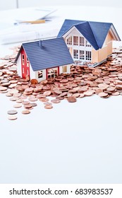 Miniatures Of Two Houses Standing Among Coins