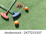 Mini-golf clubs and balls of different colors laid on artificial grass.