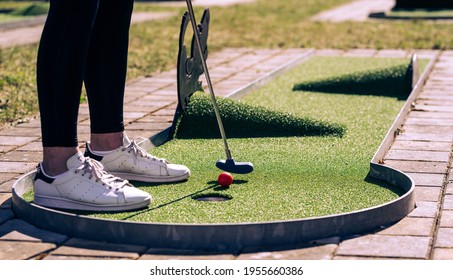 Minigolf player with white sneakers putting golf ball into the hole on bumpy green lane. 