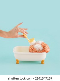 Minimal abstract psychology concept made with  young female hand brushing human brain in tub with foam, on isolated pastel aquamarine blue background. Mental health, mental wellbeing or brainwashing. - Shutterstock ID 2141547159