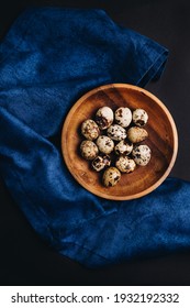 Minimal art of fresh quail eggs in the wooden bowl on the dark background with blue saten or silk around. Easter table setting. - Shutterstock ID 1932192332