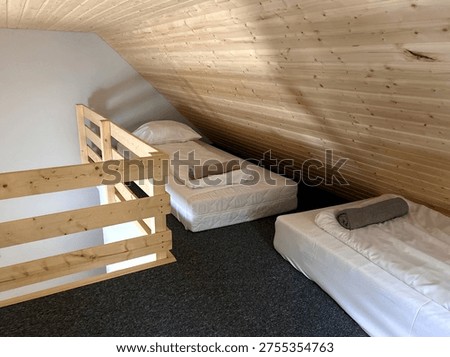 Minimal attic sleeping area with two floor mattresses under a sloped wooden ceiling in a compact loft bedroom.