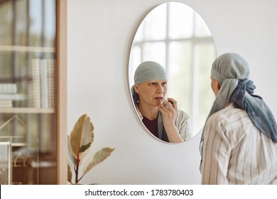Minimal Back View Portrait Of Mature Bald Woman Putting On Makeup And Lipstick While Looking In Mirror At Home, Embracing Beauty, Alopecia And Cancer Awareness, Copy Space