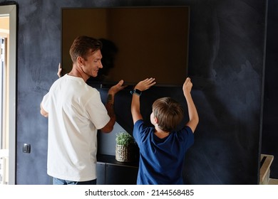 Minimal Back View Portrait Of Smiling Father And Son Hanging TV On Wall Together While Moving To New Home