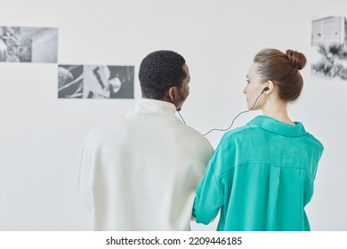 Minimal Back View Of Young Couple With Earphones Looking At Abstract Art In Museum Together, Copy Space