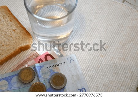 Minimal composition with bread slice, glass of water and small amount of euro money representing cost of living crisis concepts, poverty, limited resources and basic survival. Strong financial hardship symbol with Copy Space.