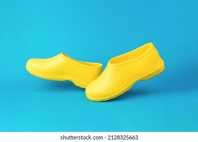 Minimal composition of bright yellow rubber galoshes on a blue background. Shoes for wet weather. Space for text.